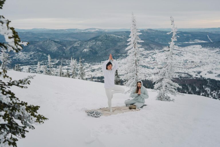 Couple practicing yoga and meditation in a snow-covered mountain landscape, embracing winter serenity.